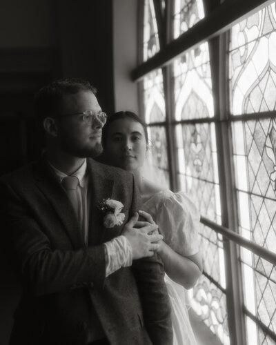Bride and groom standing by stained glass windows at Franklin Park Conservatory in Columbus, Ohio — an intimate black and white portrait captured by Rainstorm