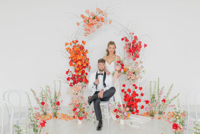 Bride and groom under bright wedding arch with red, orange and pink florals