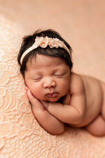 Beautiful baby girl posed on a peach backdrop with matching headband.