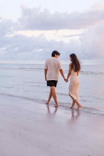 Couple walking away on the beach with blue sunset clouds