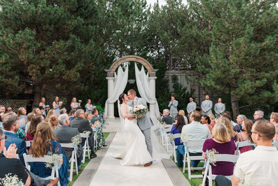 denver wedding photographer captures bride and groom holding hands as they exit their outdoor downtown denver wedding ceremony as their guests clap for them
