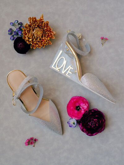 A detail flatlay of a bride's shoes for her wedding, with colorful florals all around them.