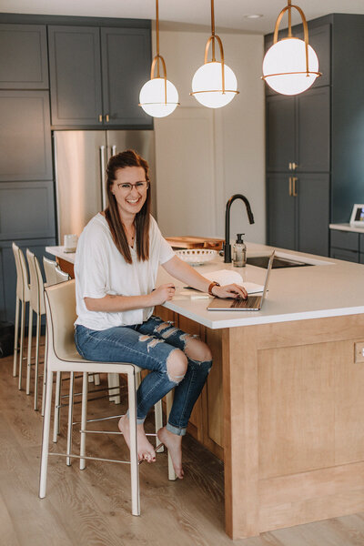 Liz Strong smiling sitting at kitchen island working on laptop