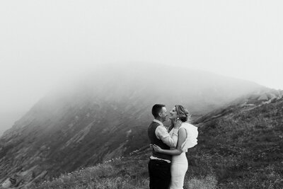 bride and groom laugh on the edge of a foggy cliff