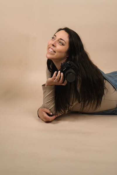 Woman laying on her stomach looking off in the distance holding her nikon camera.