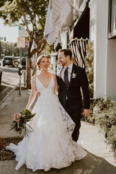 Bride and groom laugh with each other while walking down sidewalk