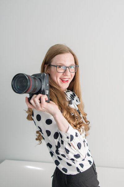 headshot of erika rene photography wearing black and white polka dots with camera in hand