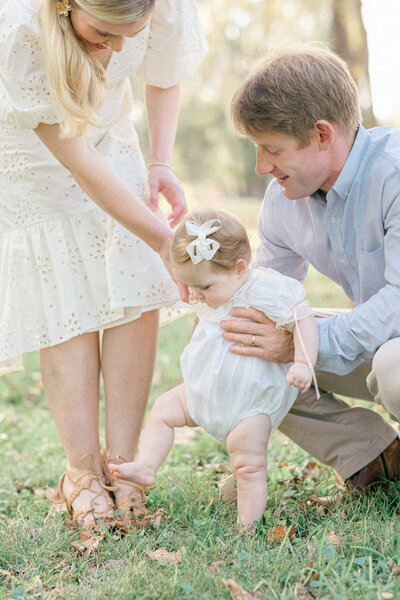 image of mom and dad helping their baby take her first step during their omaha family photography session