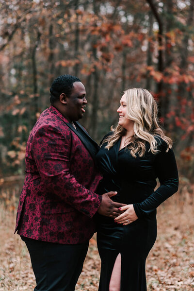 pregnant mom in black velvet smiling at her husband who's holding her belly