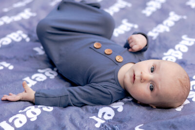 Newborn baby laying on blue blanket looking over their shoulder at the camera.