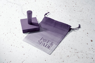 A small canvas pouch and purple brand stamp showcase the branding and packaging design for a modern, minimal landscape design business..