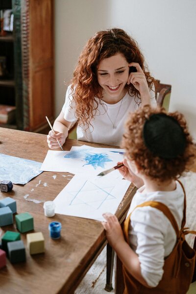 therapist smiling, assisting child in watercolor