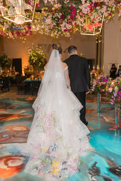 Colorful wedding reception with floral dance floor, bride and groom facing away but viewing the room for first time, beautiful colorful florals hanging with gold lanterns