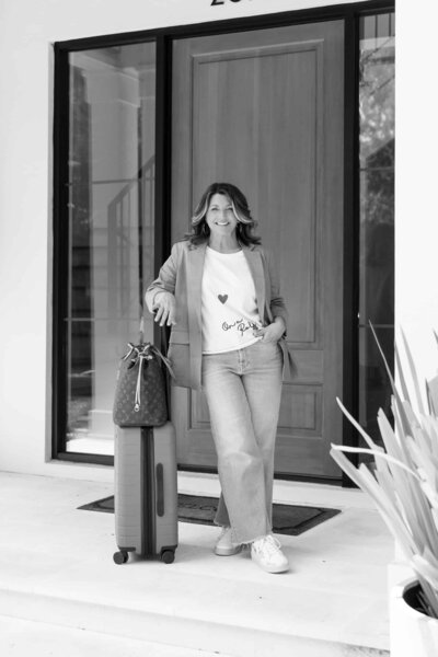 woman standing in front of a door with a suitcase and purse