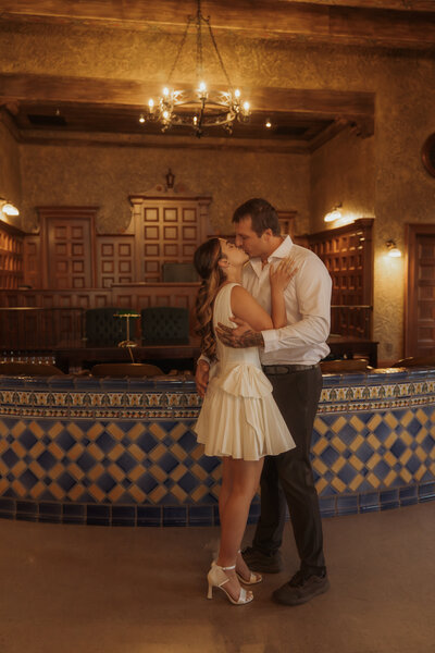 Bride and groom sharing a cinematic dip kiss in front of a charming white chapel, bride in a flowing gown and groom in a navy suit on a sunny Texas day.