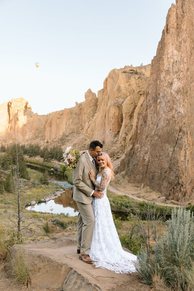 Couple embracing with a hot air balloon behind them at Smith Rock State Park.