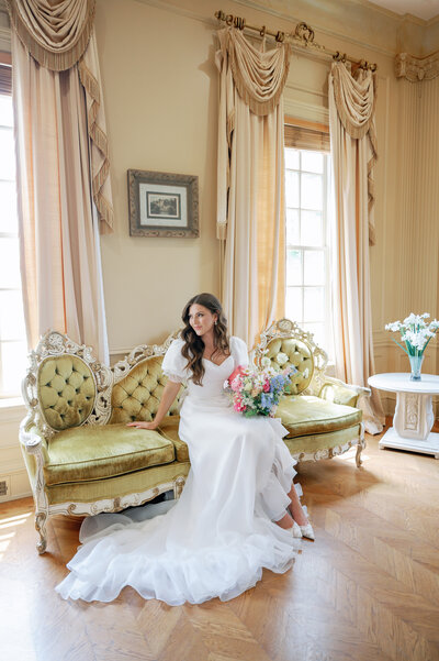 Bride sitting on sofa with bouquet 