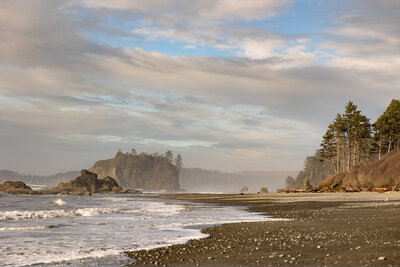 Bride and groom walking hand in hand with bouquet along a lake shore.