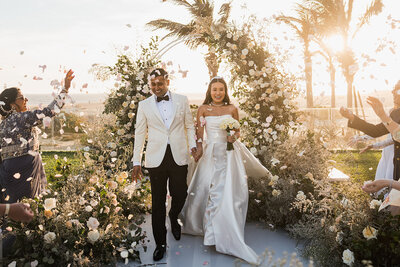 bride and groom holding hands walking underneath flower arch