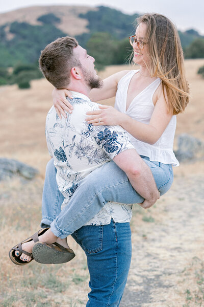 outdoor engagement session with man carrying woman in a field in Sonoma as they smile and laugh together captured by bay area photographers