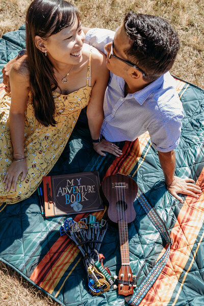 Engaged couple smile while having a picnic during engagement portrait session