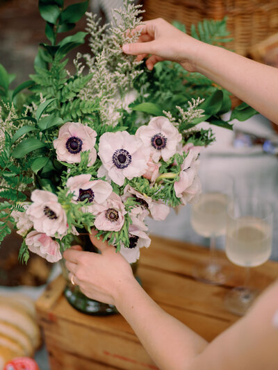 A person makes a floral arrangement with white and purple flowers.