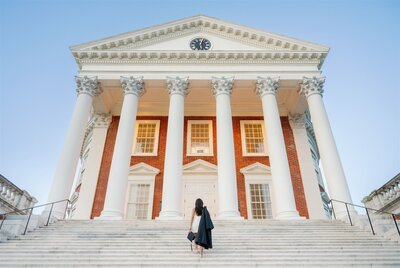 woman wearing white holding her cap and gown standing on steps of UVA Rotunda