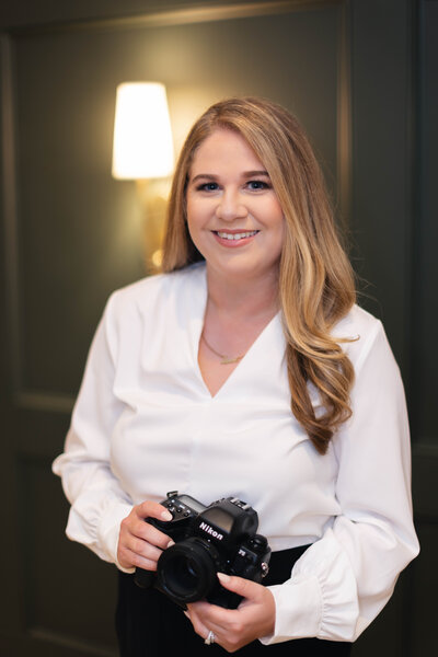 Calista smiling in a white blouse while holding a camera