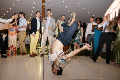 A person sliding on their head as they dance at a wedding reception 