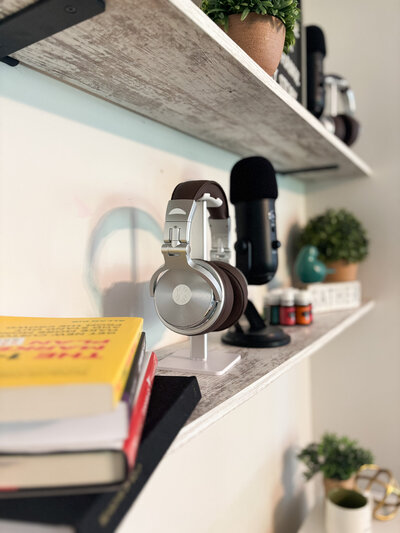 Studio shelf with headphones, microphone, books, and potted plants in a cozy creative space.