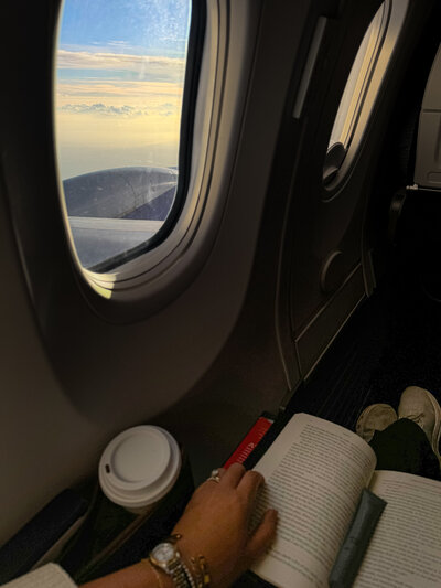 View from an airplane window with a coffee cup in hand, representing upcoming wellness retreats for women seeking immersive rest, reconnection, and renewal in supportive community.