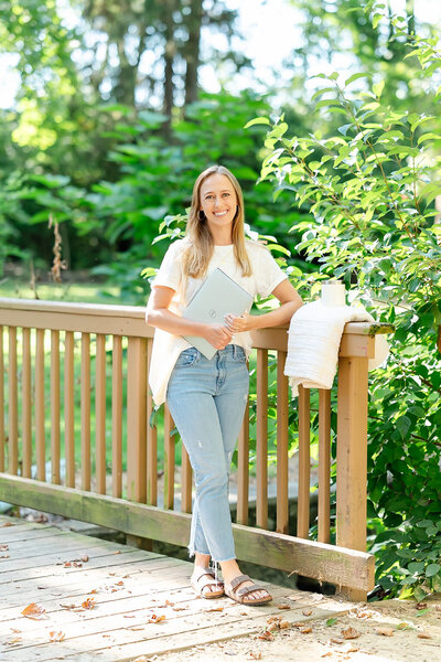 Emily Howell holding her laptop, smiling at the camera while standing near a bridge in a park