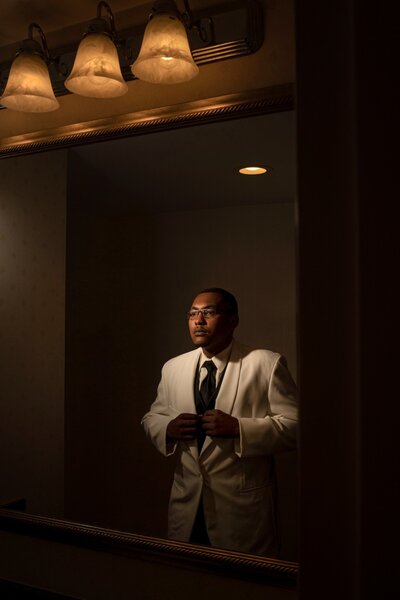 Groom getting ready for his wedding at Omni Severin Hotel in downtown Indianapolis, adjusting his suit in the mirror with warm lighting