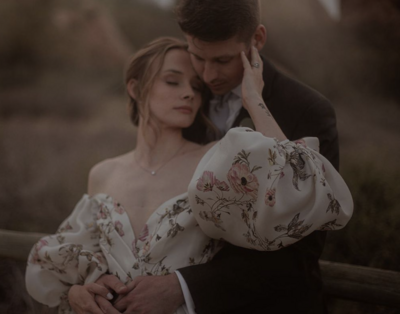 A man holds a woman from behind. The woman's head is nestled next to the man's and her hand is touching the side of his face. 