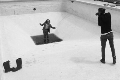 Behind the scenes musician photoshoot Ben Caplan standing in puddle in drained pool while Mark photographs him black and white image
