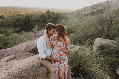 A couple cuddle together at Enchanted Rock during a maternity photo session