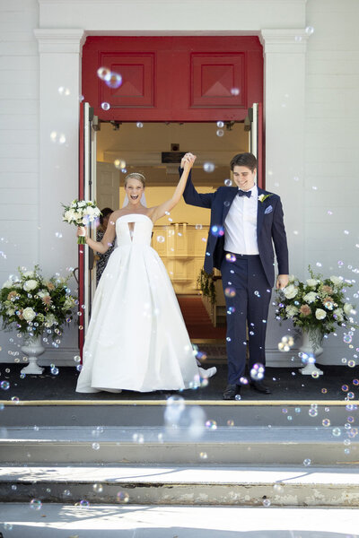 A jubilant couple exits the church after their wedding ceremony to a cloud of bubbles