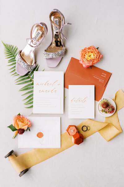 Flat lay of wedding invitations with flowers, shoes, and rings