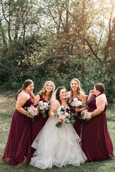 Bride with bridesmaids wearing maroon and laughing