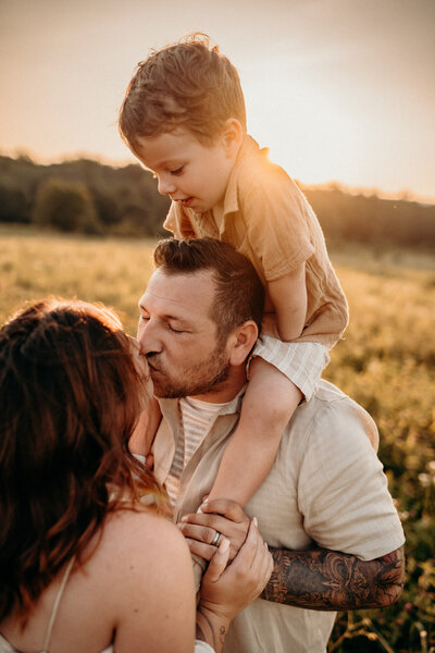 family photos- dad kissing mom with son on his shoulder 