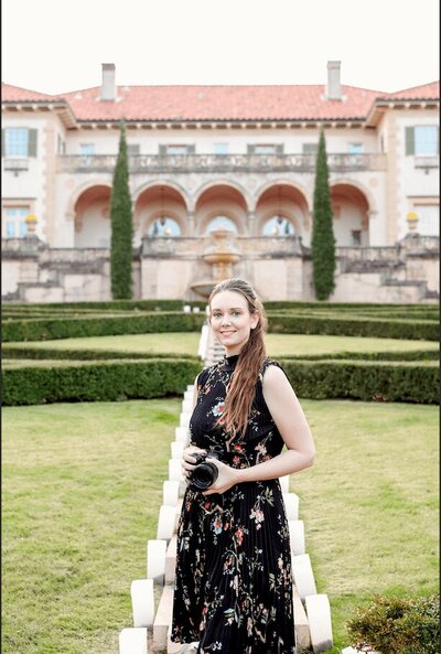 woman standing in front of the philbrook museum outside holding a camera and smiling