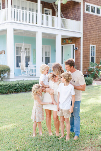 Family smiling at each other while standing in front of their island home during family photos