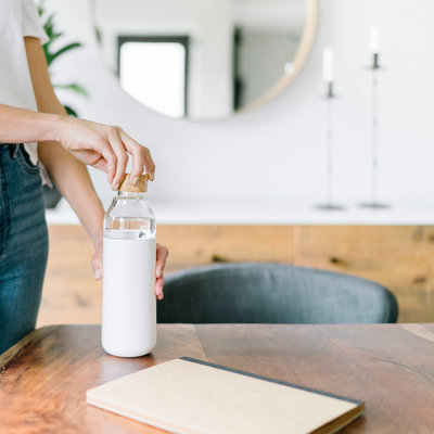 Woman holding a white water bottle at a desk with notebook, in a minimalist home office