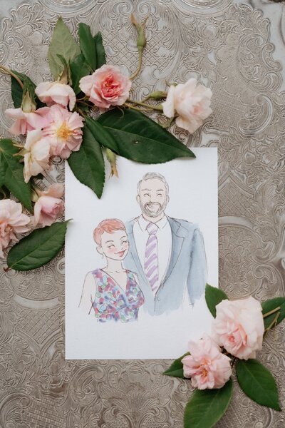 A watercolor portrait of a smiling couple, surrounded by soft pink flowers and green leaves, set against an elegant silver background.