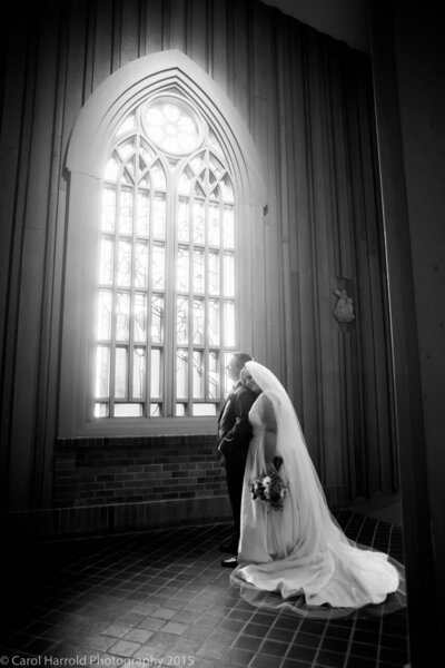 Bride and groom embrace in front of stained glass window