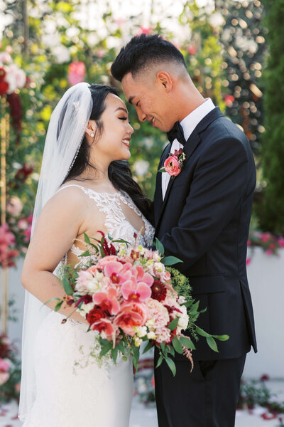 Bride and Groom holding vibrant bridal bouquet standing in front of their floral ceremony backdrop