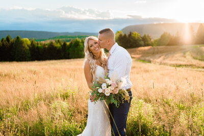 Groom kissing bride in a meadow at sunset during their golden hour bridal portraits