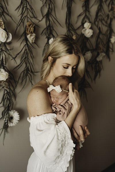 A mom holds tight and takes in all the sweet smells of her newborn baby girl during a sweet and tender moment of their bismarck in-home newborn session.