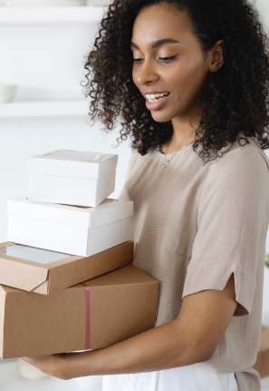 Woman with black, curly hair and a medium skin tone is carrying a pile of boxes