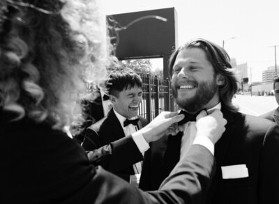 Groomsman fixing groom tie by best candid wedding photographers Noble Photo Co